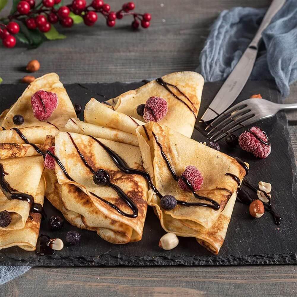 Delicious crepes topped with berries and chocolate sauce on a slate plate, perfect for brunch or dessert.